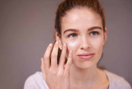 Shot of a teenager applying moisturizer to her