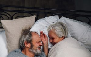 älteres Paar liegt zusammen im Bett und lächelt sich an