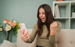 Frau feiert, dass sie eine Sportwette gewonnen hat, während sie das Ergebnis auf einem Smartphone-App. Glückliche Wetten für Frauen in einem Online-Casino mit einem Handy. Eine aufgeregte Dame, die den Lottogewinn sieht