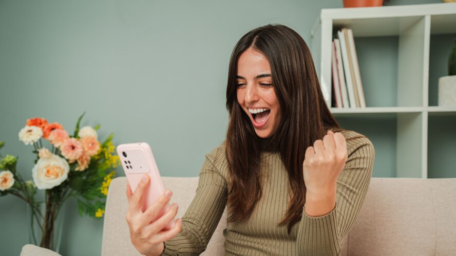 Frau feiert, dass sie eine Sportwette gewonnen hat, während sie das Ergebnis auf einem Smartphone-App. Glückliche Wetten für Frauen in einem Online-Casino mit einem Handy. Eine aufgeregte Dame, die den Lottogewinn sieht