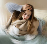 Kranke junge weiße Frau, die aus dem Bett steigt, ihren Kopf aufgrund von Schwindel, Migräne, Schwindel, Kopfschmerzen im Schlafzimmer zu Hause hält. Saisonale Kälteerscheinungen, Grippeepidemie, Fieber, Krankheit, Krankheit, Unwohlsein.