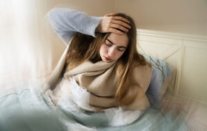 Kranke junge weiße Frau, die aus dem Bett steigt, ihren Kopf aufgrund von Schwindel, Migräne, Schwindel, Kopfschmerzen im Schlafzimmer zu Hause hält. Saisonale Kälteerscheinungen, Grippeepidemie, Fieber, Krankheit, Krankheit, Unwohlsein.