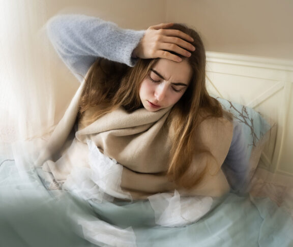 Kranke junge weiße Frau, die aus dem Bett steigt, ihren Kopf aufgrund von Schwindel, Migräne, Schwindel, Kopfschmerzen im Schlafzimmer zu Hause hält. Saisonale Kälteerscheinungen, Grippeepidemie, Fieber, Krankheit, Krankheit, Unwohlsein.