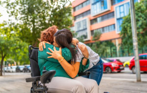 Zarter Moment einer kaukasischen Frau mit Behinderung, die ihre asiatische Betreuerin in der Stadt umarmt