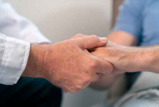 Arzt, der die Hände hält und den männlichen Patienten beruhigt. Medizinische Gesundheitsversorgung, Krankheitsdiagnose und Unterstützung bei der Kommunikation mit Empathie. Gesundheitstherapie, Psychotherapie, Wellnessberatung in der Klinik.