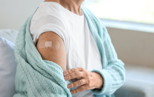 Seniorin mit Pflaster sitzt nach Impfung zu Hause auf dem Sofa, Nahaufnahme