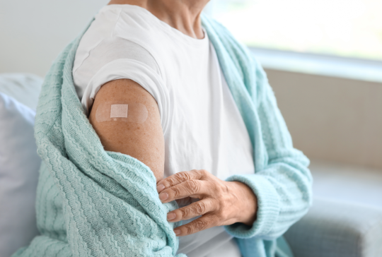 Seniorin mit Pflaster sitzt nach Impfung zu Hause auf dem Sofa, Nahaufnahme