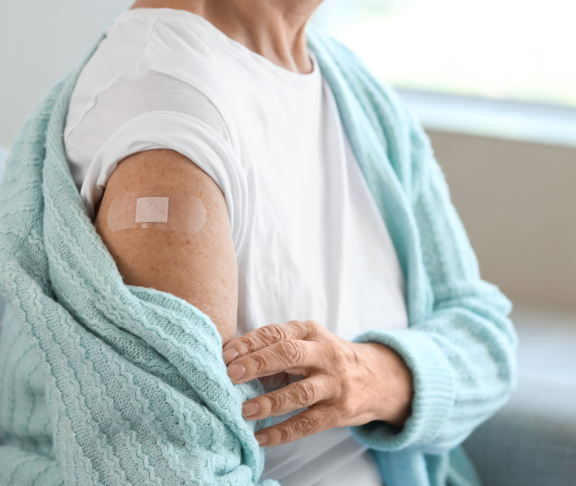 Seniorin mit Pflaster sitzt nach Impfung zu Hause auf dem Sofa, Nahaufnahme