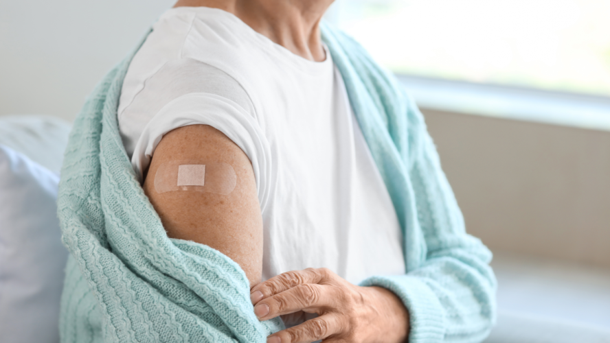 Seniorin mit Pflaster sitzt nach Impfung zu Hause auf dem Sofa, Nahaufnahme