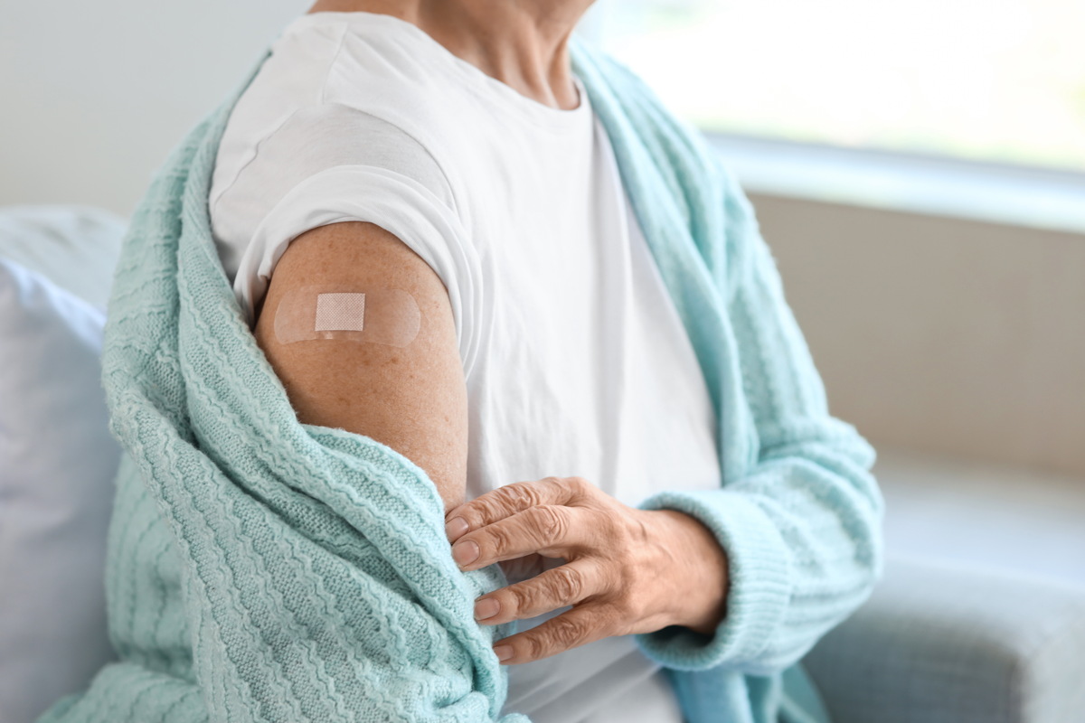 Seniorin mit Pflaster sitzt nach Impfung zu Hause auf dem Sofa, Nahaufnahme