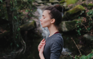 Junge Frau, die im Mooswald auf dem Hintergrund des Wasserfalls Yoga pranayama draußen atmet. Einheit mit Naturkonzept