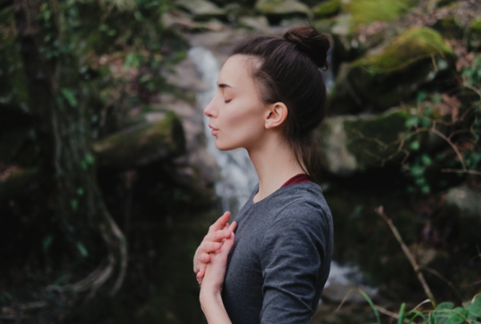 Junge Frau, die im Mooswald auf dem Hintergrund des Wasserfalls Yoga pranayama draußen atmet. Einheit mit Naturkonzept