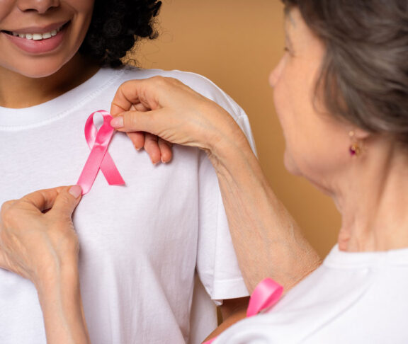 Hochrangige Freiwillige tragen auf dem weißen T-Shirt einer lächelnden jungen Frau ein rosafarbenes Band auf, das Einheit und Unterstützung für das Bewusstsein für Brustkrebs symbolisiert, Hoffnung fördert und die Früherkennung fördert. Support-Konzept