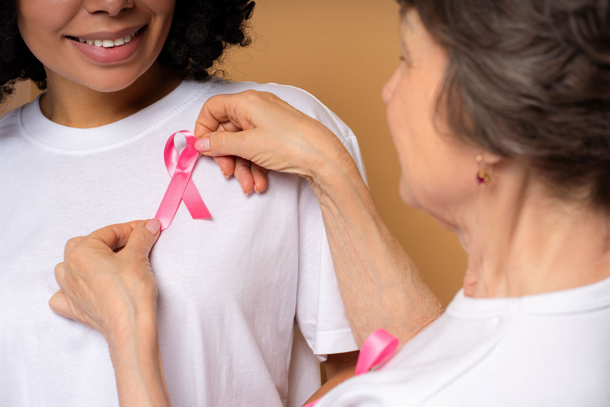 Hochrangige Freiwillige tragen auf dem weißen T-Shirt einer lächelnden jungen Frau ein rosafarbenes Band auf, das Einheit und Unterstützung für das Bewusstsein für Brustkrebs symbolisiert, Hoffnung fördert und die Früherkennung fördert. Support-Konzept