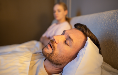Mann schlafend im Bett und schnarchen laut, während frustrierte Frau neben sitzen mit erschöpften Ausdruck, gestresste Frau verliert Schlaf wegen Ehemann schnarcht in der Nacht, Gesundheit und Beziehungen Probleme.