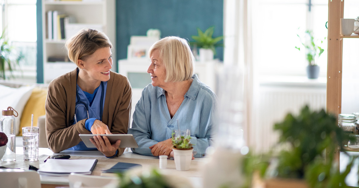 Caregiver or healthcare worker with senior woman patient, using tablet and explaining.