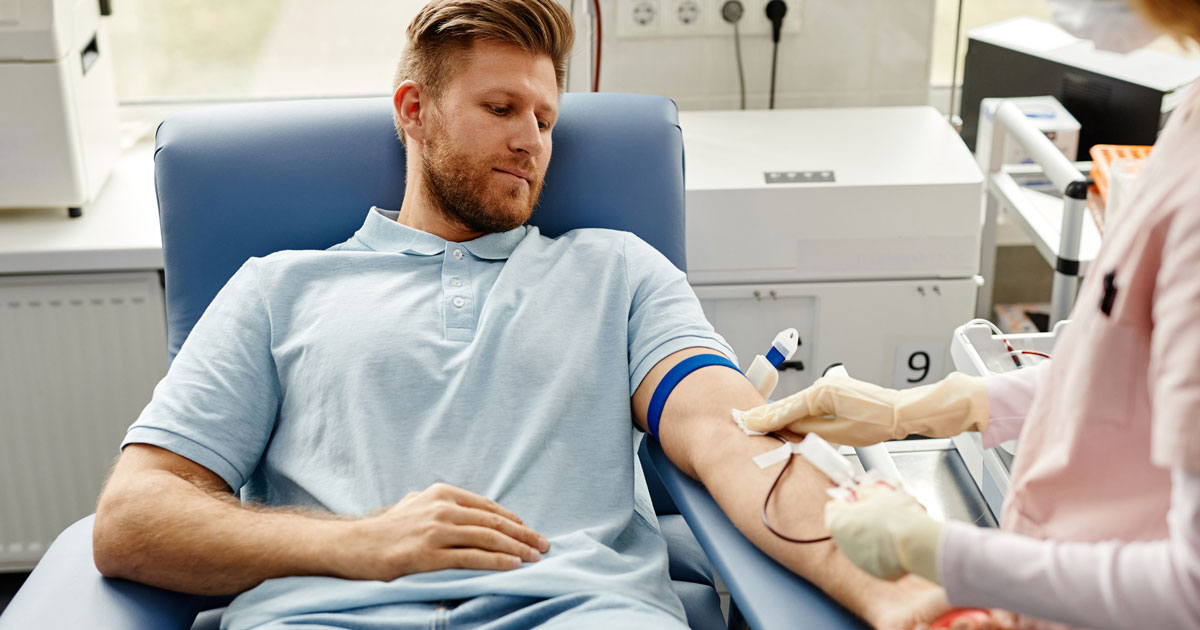 Portrait of handsome young man preparing for blood donation at med center with nurse helping