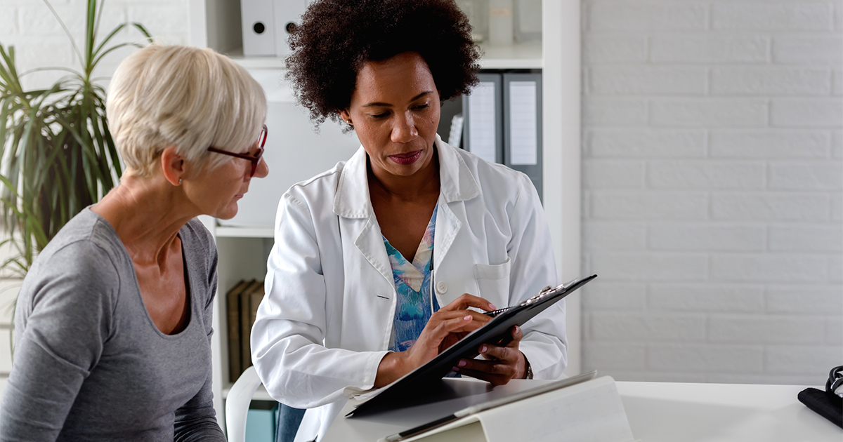 A female doctor sits at her desk and chats to an elderly female patient while looking at her test results