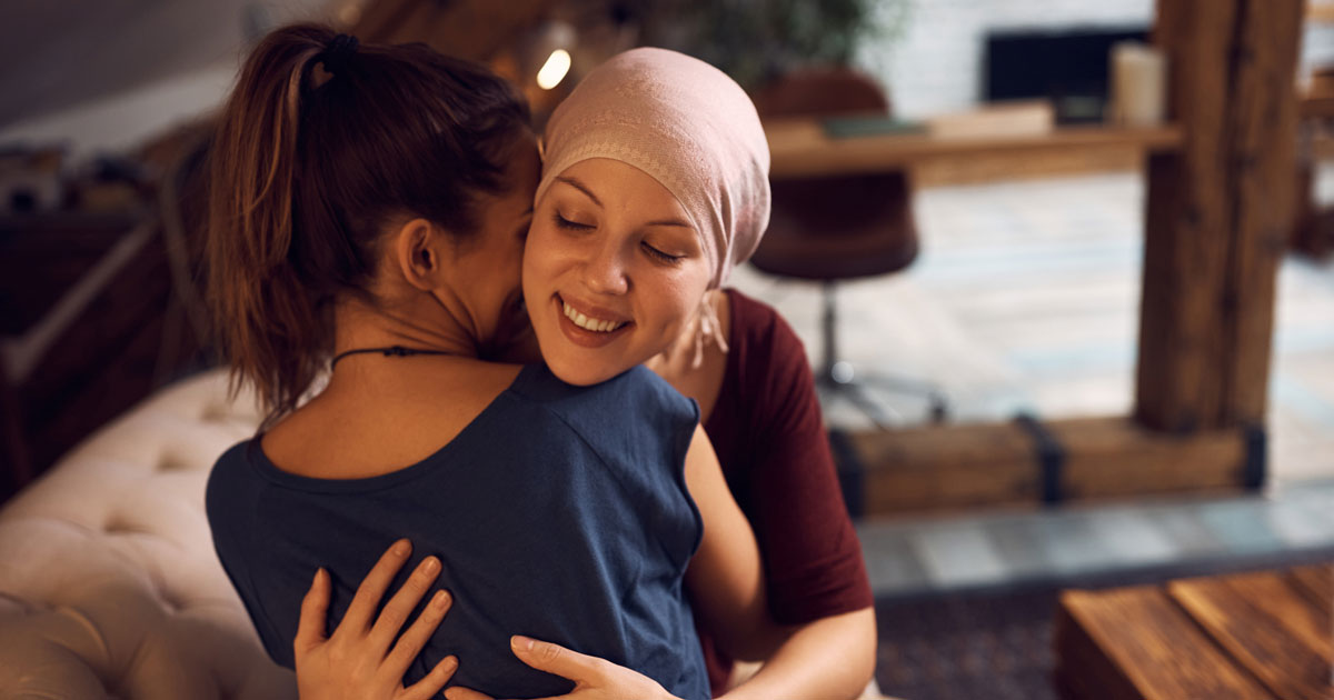 Happy cancer patient embracing her friend who is visiting her at home.