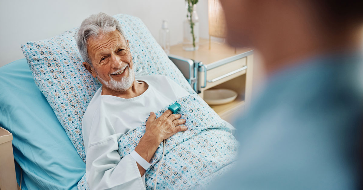 Happy senior patient talking to a nurse while recovering in the hospital ward.