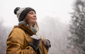 Young mature adult caucasian woman in a hat and yellow jacket breathing fresh air in the winter forest