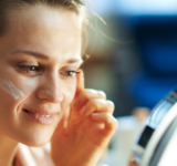 Elegant female applying facial cream and looking in mirror
