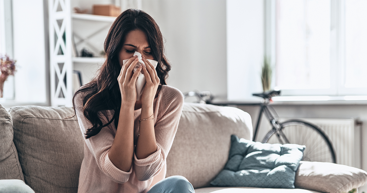 ick young woman blowing the nose using tissue paper while sitting on the sofa at home