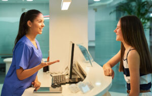 Medical, reception and nurse with patient in hospital for advice, help and information. Medicine, happy and healthcare with women at desk in clinic for nursing, waiting room and service