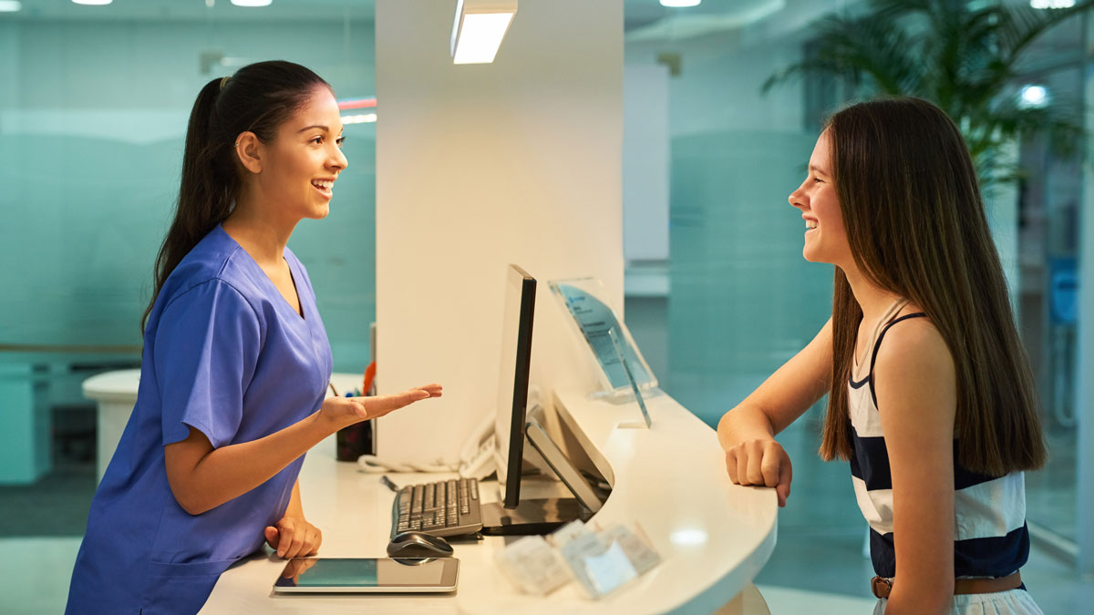Medical, reception and nurse with patient in hospital for advice, help and information. Medicine, happy and healthcare with women at desk in clinic for nursing, waiting room and service