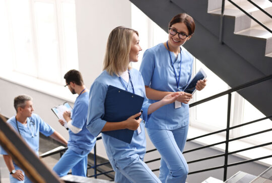Healthcare workers with tablet and clipboard walking up stairs in hospital