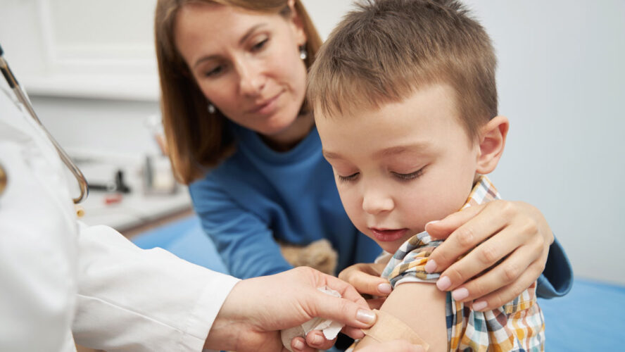 Doctor placing medical plaster on child arm after vaccination