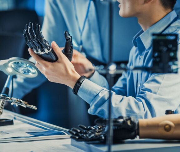 Technological Prosthetic Robot Arm is Tested by Two Professional Development Engineers in a High Tech Research Laboratory with Modern Futuristic Equipment. Compare Data on a Personal Computer.