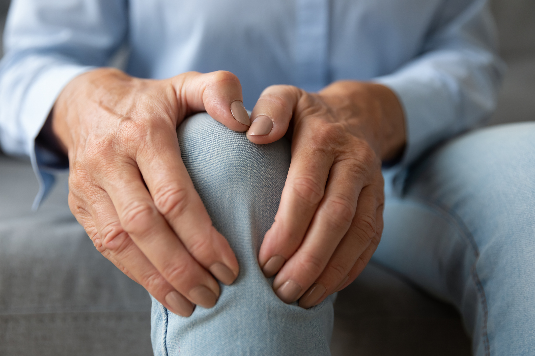 Old senior adult woman female hands touching knee sitting alone, retired elderly grandma feeling hurt joint pain in leg suffering from osteoarthritis bones disease or injury concept, close up view