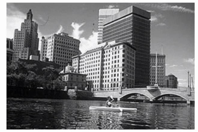 Original black-and-white photograph of a riverside city skyline with a rower on the water