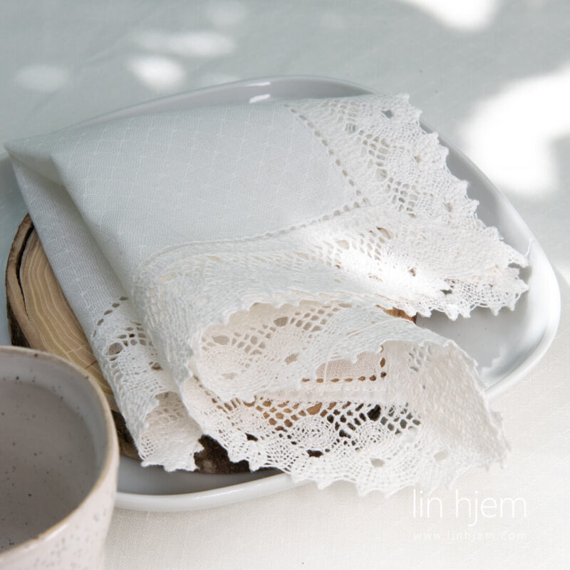 Hullm&oslash;nstret hvit serviett i lin med blonder.