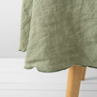 Rund grønnaktig lin duk med dekorativ tett grønn søm rundt