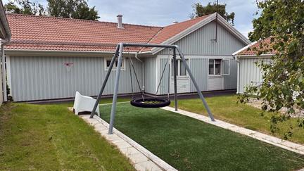 En gunga på en gräsmatta med ett grått trähus bakom.