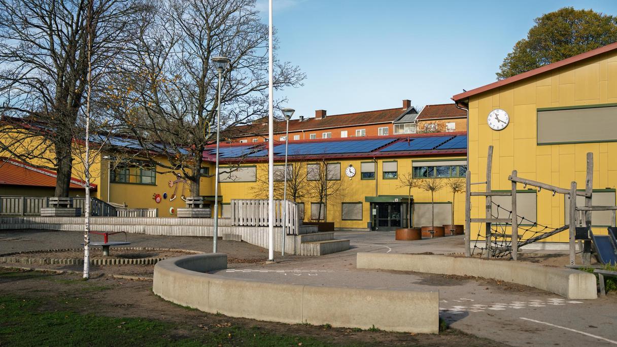 En gul skolbyggnad med en klocka på fasaden.