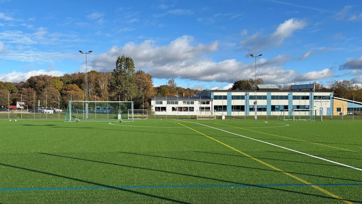 En grön fotbollsplan med byggnader i bakgrunden.