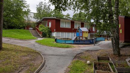 Bilden föreställer en röd byggnad och en förskolegård med en klätterställning med en ruschkana.