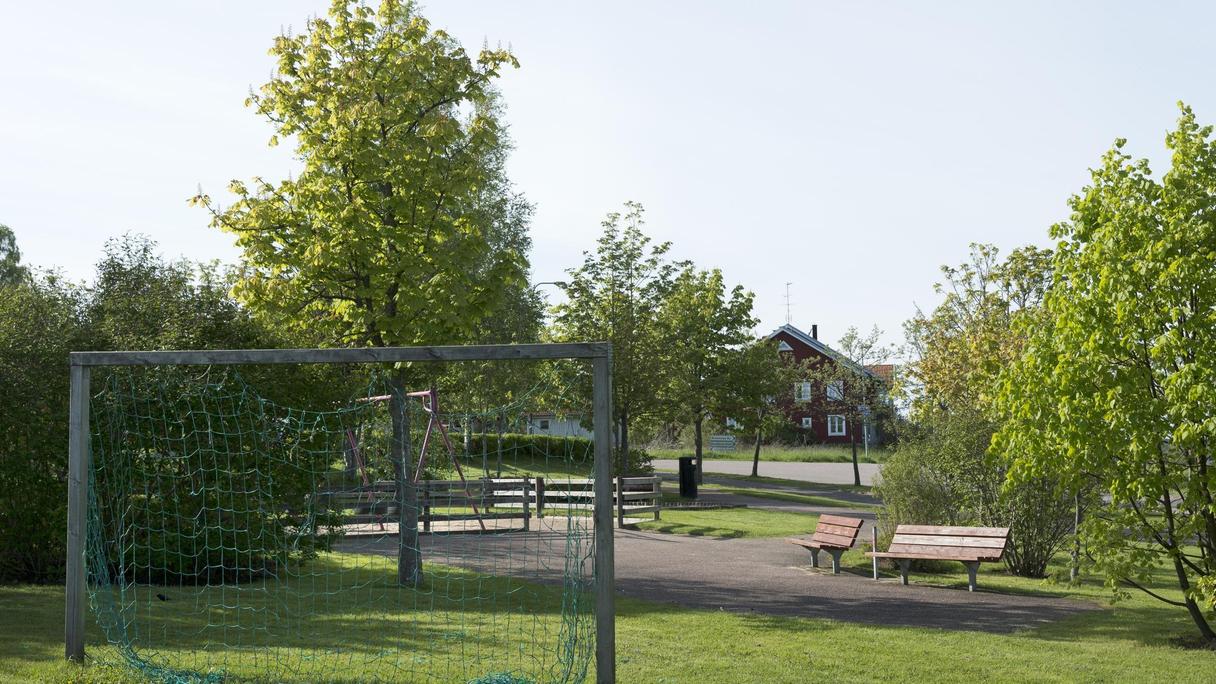 Yta av gräs och asfalt med bland annat ett fotbollsmål och gungställning.