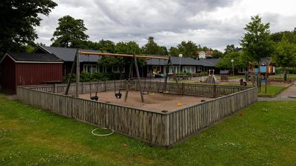 Bilden föreställer en röd byggnad och en förskolegård med gungor och klätterställningar.