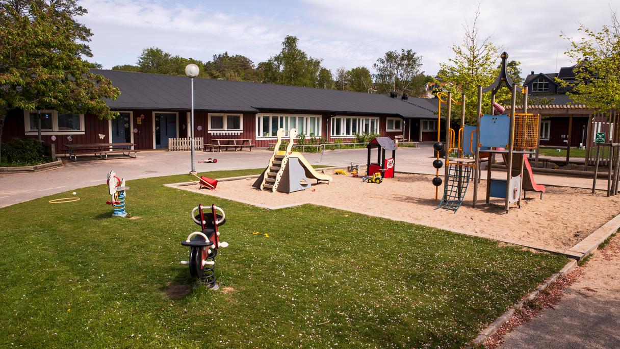 Röd förskolebyggnad med lekplats framför.