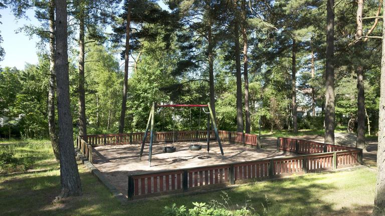 Skogsmiljö med en sandlåda och gungställning.