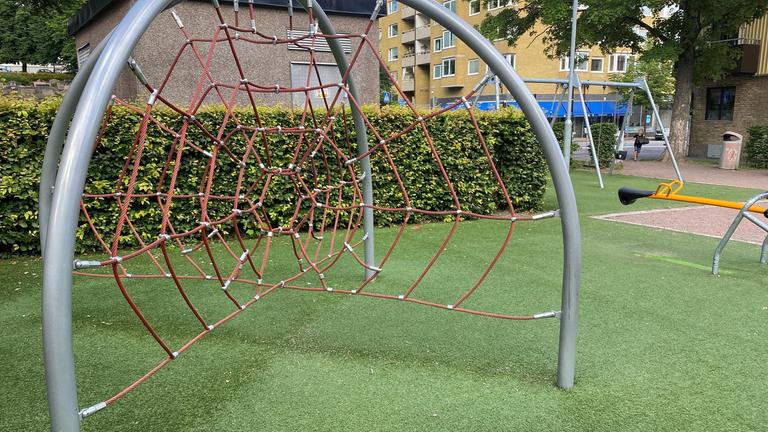Lekplats med konstgräs som underlag med klätterställning i förgrunden och häckar runt om