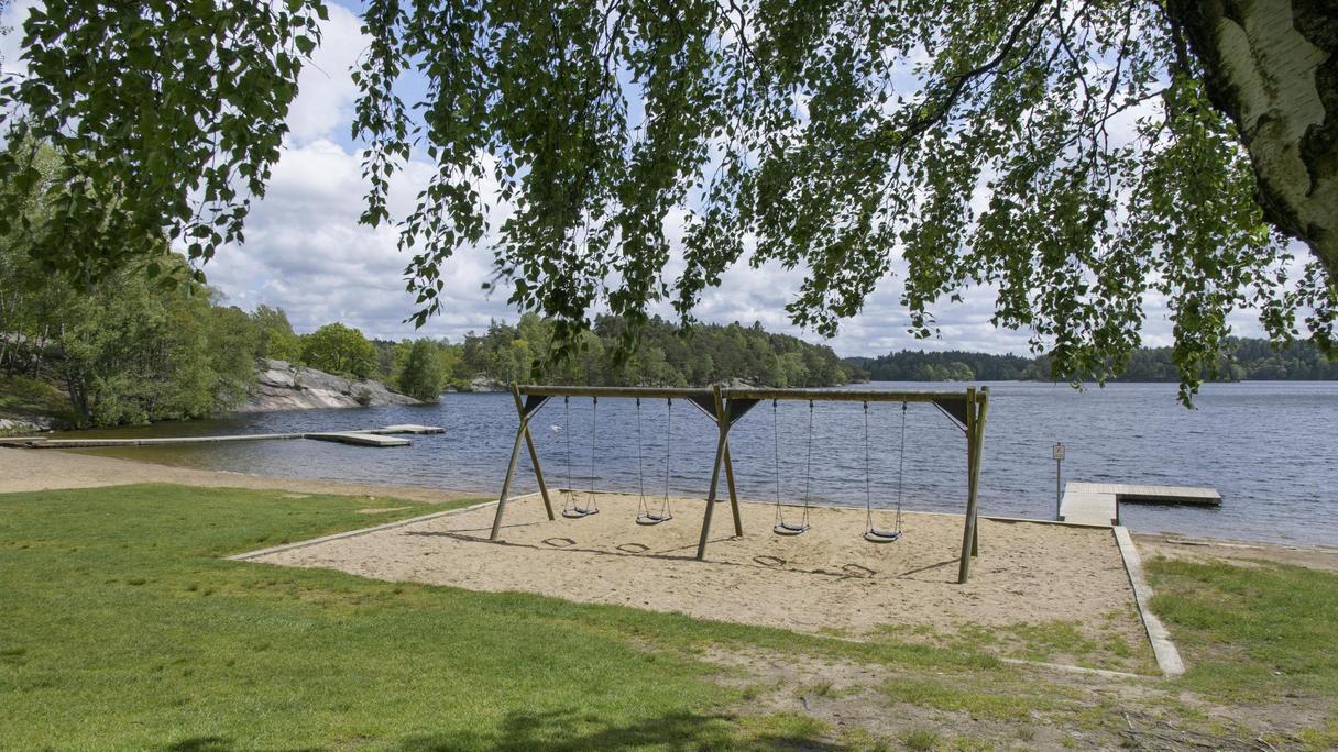 Sandlåda med gungställning framför en sjö.