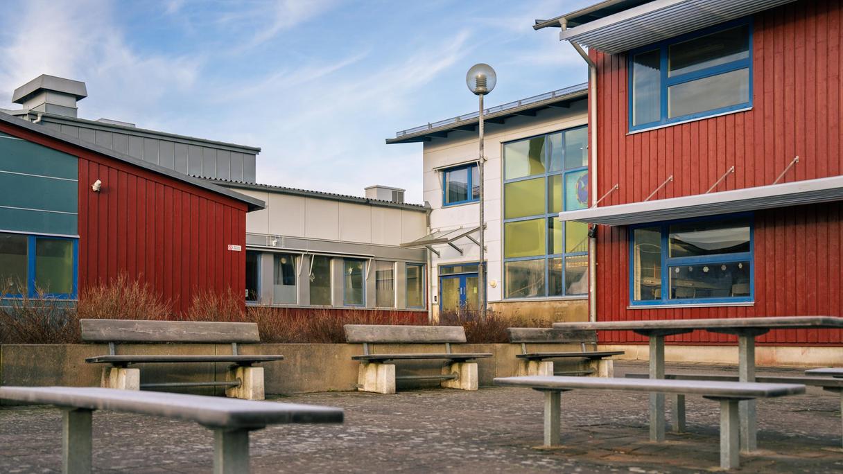 En rad bänkar framför en röd och vit skolbyggnad.