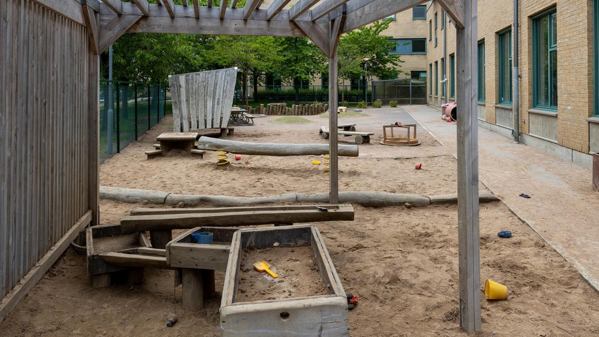 förskolegårdens pergola, stora sandlåda och leksaker. balansstock, picknickbord och liten karusell