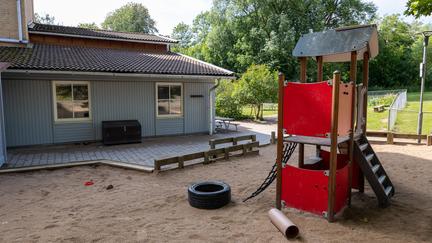 Bilden föreställer en ljusblå byggnad och en lekplats med ett däck och en röd klätterställning.