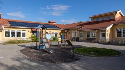 Bilden föreställer en gul byggnad med vita fönsterkarmar. Framför byggnaden finns en klätterställning med ruschkana. 